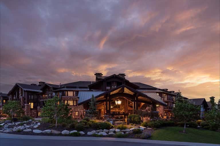 Luxury lodge exterior at dusk with wooden beams, stone accents, and illuminated entrance