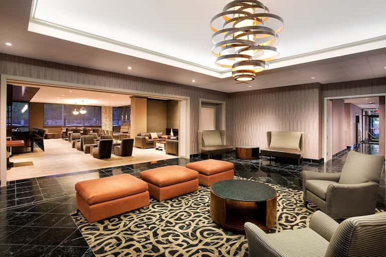 Elegant hotel lobby lounge with orange ottomans, patterned carpet, and modern chandelier