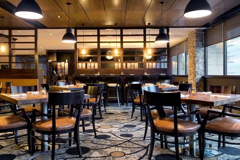 Contemporary restaurant interior with dark pendant lights, wood ceiling, black chairs, and stone accents