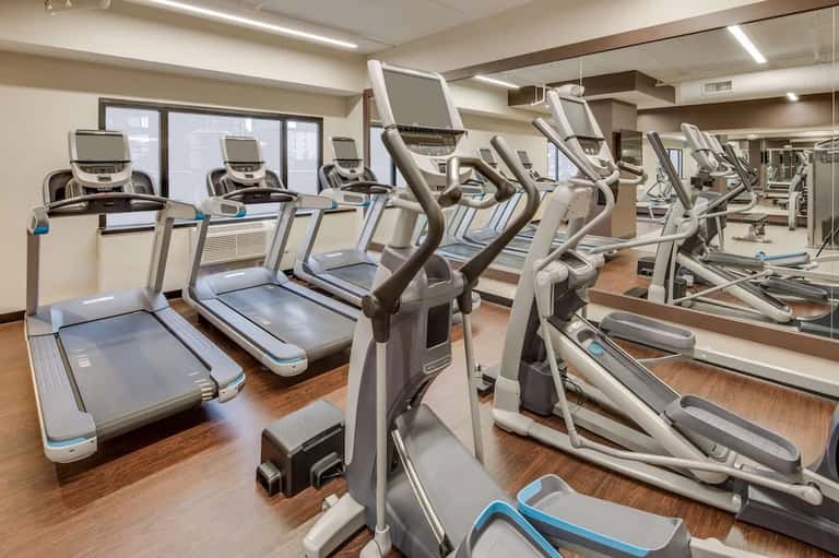 Cardio exercise room with treadmills and elliptical machines facing mirrors and large windows