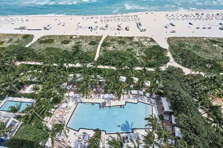 Aerial view of beachfront resort pool surrounded by palm trees with ocean and beach beyond