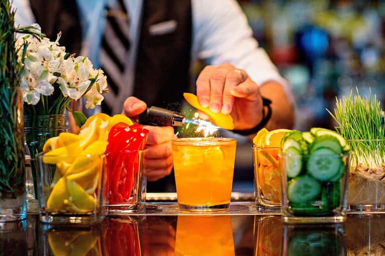 Colorful cocktails being prepared at a bar with fresh citrus garnishes and flowers