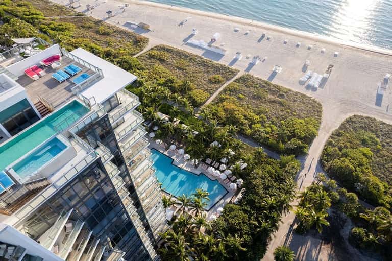 Aerial view of beachfront resort with multiple pools, sun loungers, lush tropical vegetation, and ocean access