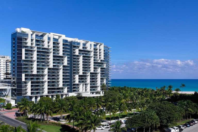 Beachfront high-rise residential building with balconies overlooking palm trees and turquoise ocean