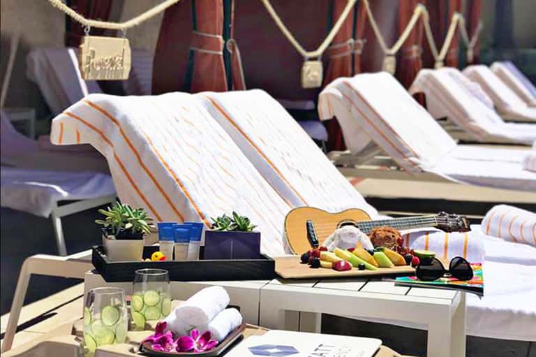 Luxury poolside lounge area with striped towels, fresh fruit, guitar, and ocean view