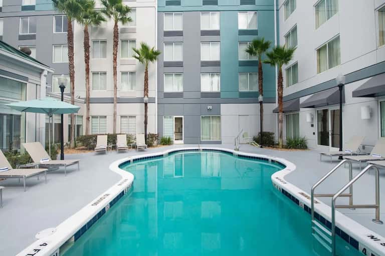 Contemporary hotel courtyard with turquoise lap pool, palm trees, and modern multi-story building