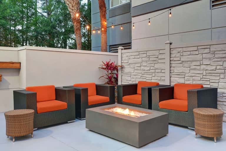 Outdoor patio with fire pit, orange cushioned seating, wicker ottomans, and contemporary architectural design