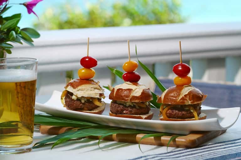 Three gourmet sliders with cherry tomato garnish and beer by pool