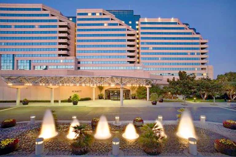 Modern multi-story hotel with pink and blue facade, illuminated fountains in courtyard at dusk