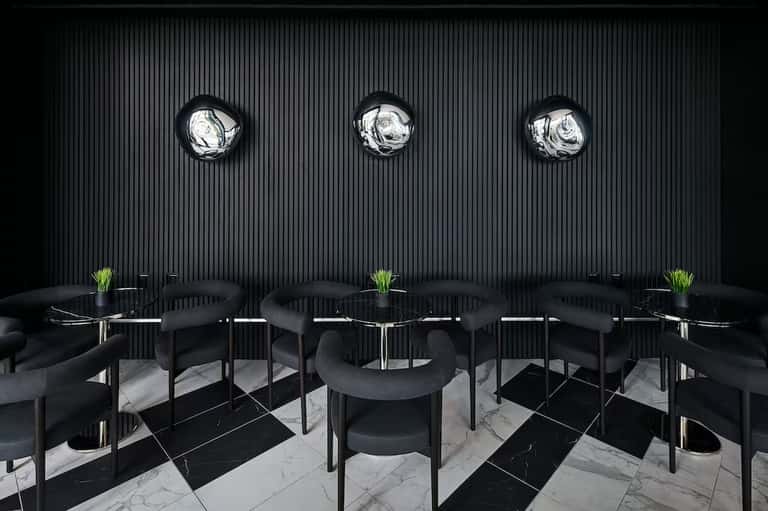 Minimalist dining space with black tables, curved black chairs, marble flooring, and circular wall sconces