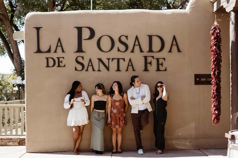 Five guests posing in front of La Posada de Santa Fe sign on stucco wall