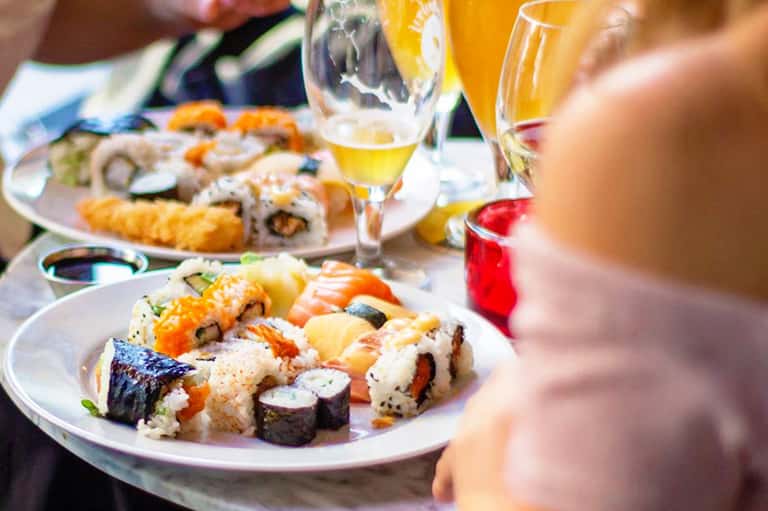 Assorted sushi rolls and nigiri on white plates with beverages at an outdoor dining table