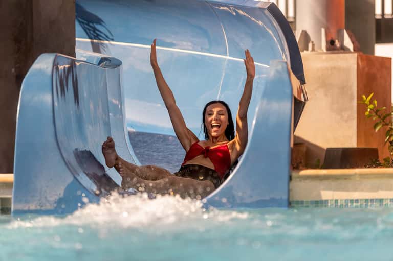 Child joyfully sliding down water slide into bright turquoise pool at resort