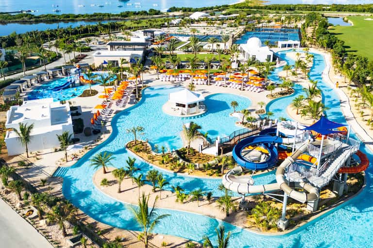 Aerial view of large resort water park with multiple pools, water slides, palm trees, and recreational facilities