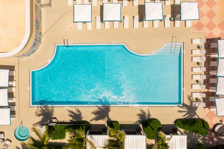 Aerial view of rectangular resort pool surrounded by lounge chairs and palm tree landscaping on sandy deck