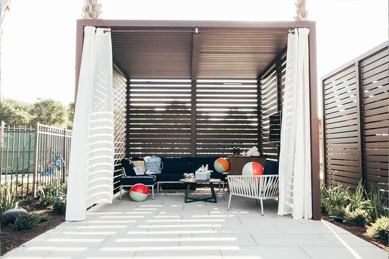 Modern outdoor pavilion with lounge seating, fire pit, and white curtains under a metal pergola