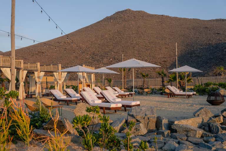 Beach resort with lounge chairs, umbrellas, and mountain backdrop at golden hour