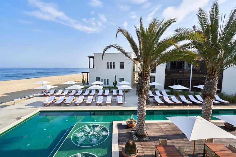 Beachfront resort with pool, palm trees, white building, and ocean view