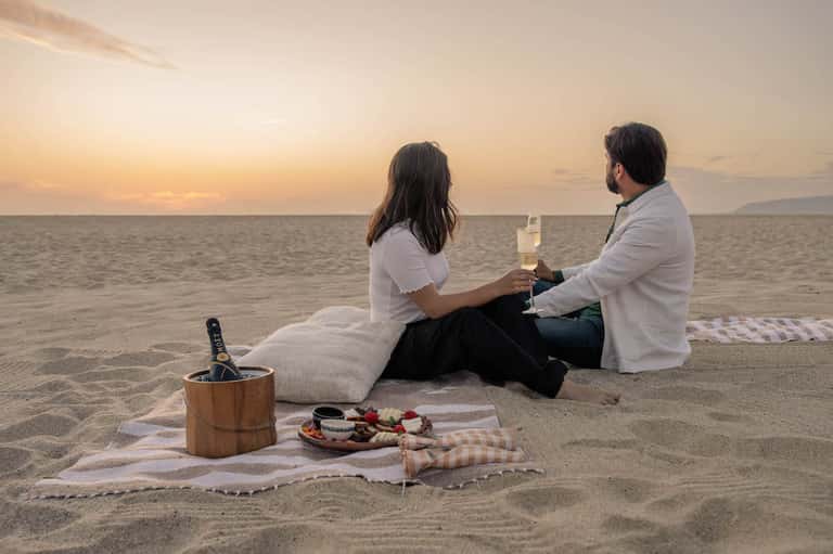 Couple enjoying champagne on beach at sunset with charcuterie board and ice bucket