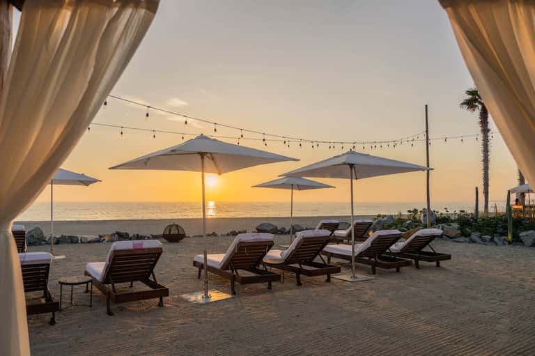 Beach sunset with lounge chairs, umbrellas, string lights, and ocean view at golden hour
