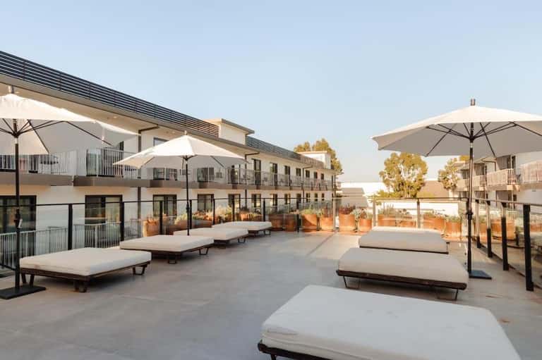 Modern rooftop terrace with lounge beds, white umbrellas, and desert landscape views