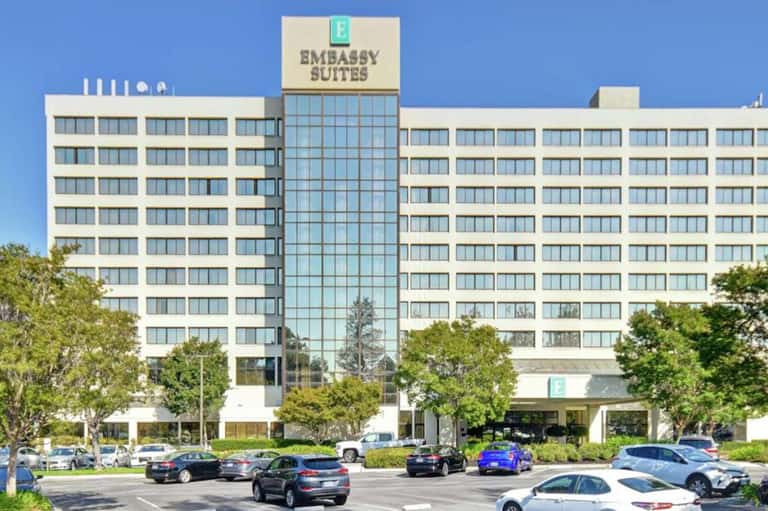 Embassy Suites hotel exterior, multi-story white building with glass center tower and parking lot
