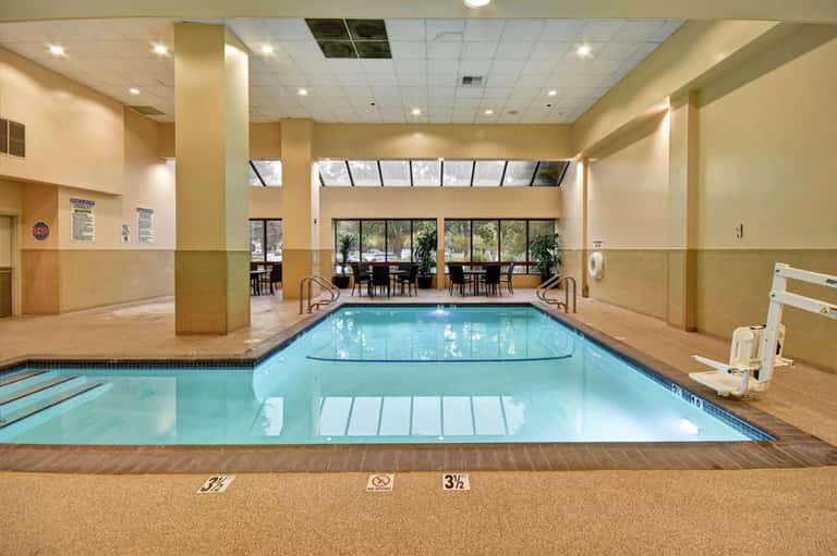 Indoor swimming pool with lane markers, beige walls, columns, and windows overlooking outdoor seating area