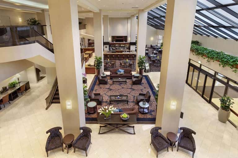 Multi-level hotel lobby atrium with seating areas, bar, decorative columns, and geometric railings.