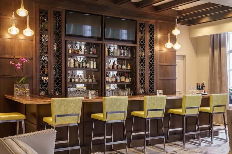Upscale hotel bar with wooden cabinetry, yellow bar stools, and illuminated pendant lights