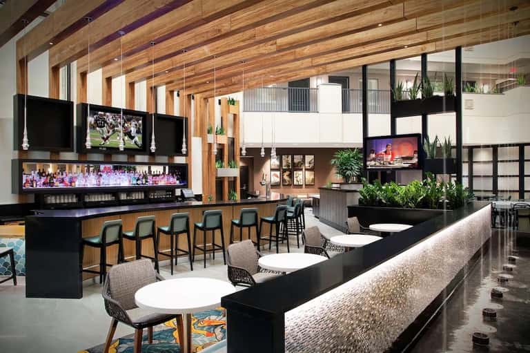 Modern hotel bar and lounge with wooden beams, black bar counter, and multiple seating areas