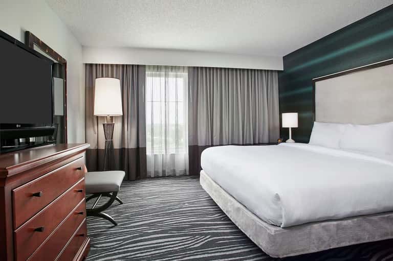 Modern hotel bedroom with queen bed, dark teal accent wall, and balcony access