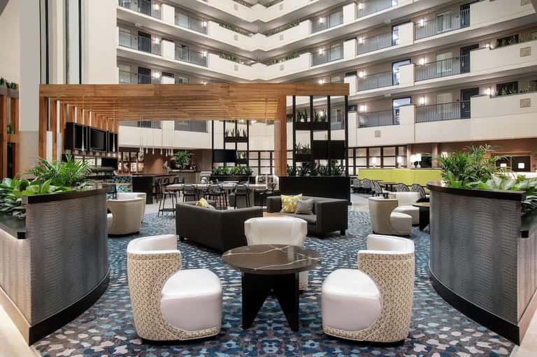 Modern hotel lobby with atrium ceiling, wooden beams, contemporary furniture, and planted urns