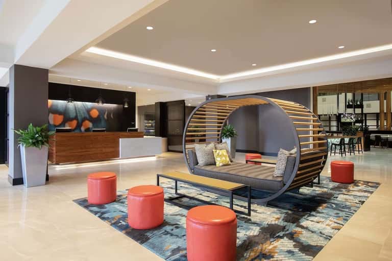 Modern hotel lobby with curved wooden pod seating, red ottomans, reception desk, and contemporary design