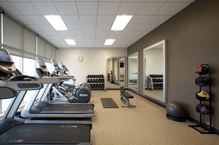 Fitness center with treadmills, elliptical machines, dumbbells, and mirrored walls