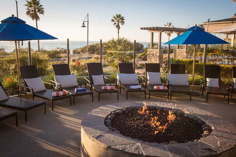 Beachfront fire pit lounge with blue umbrellas, lounge chairs, and ocean view