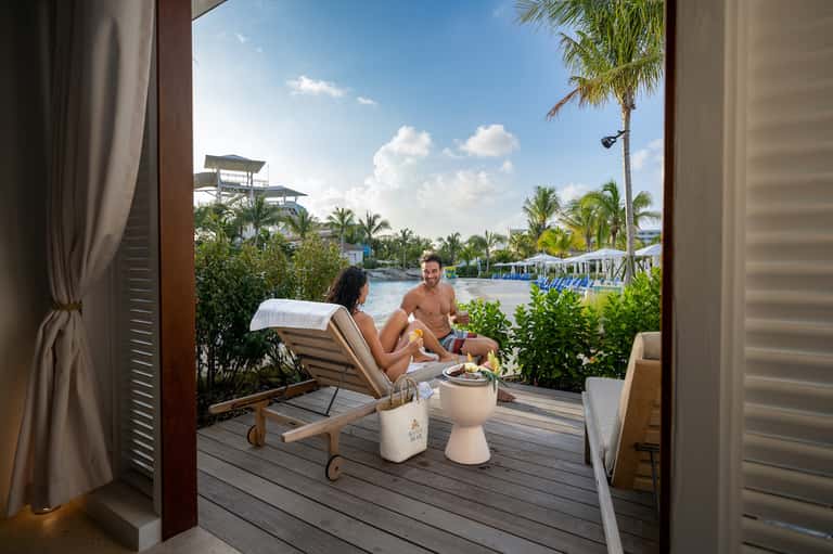 Couple relaxing on a waterfront deck with lounge chairs overlooking a tropical resort landscape