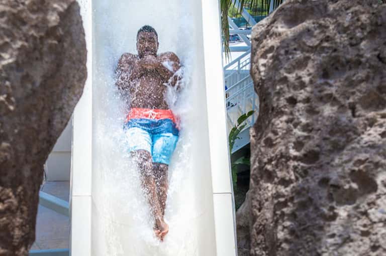 Person sliding down white water slide between rock formations at tropical resort