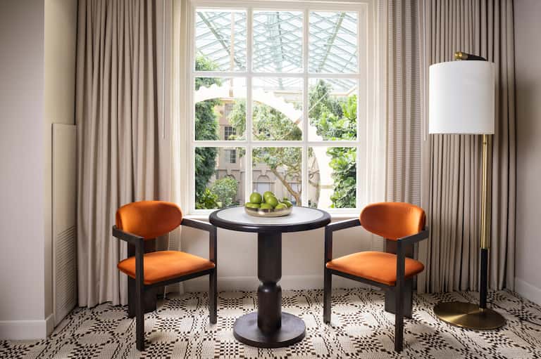 Elegant seating nook with orange velvet chairs, round black table, and large windows overlooking trees