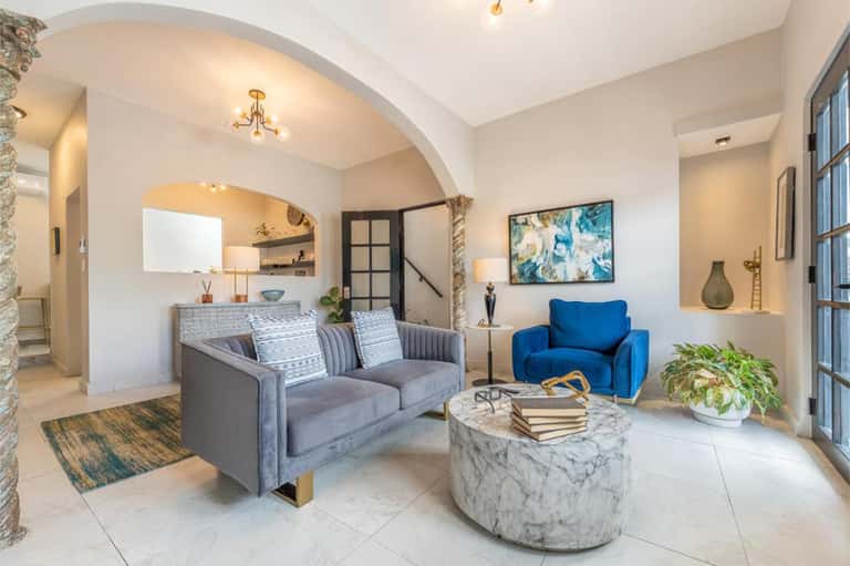 Modern residential lobby with arched ceiling, gray sofa, blue chair, and marble coffee table