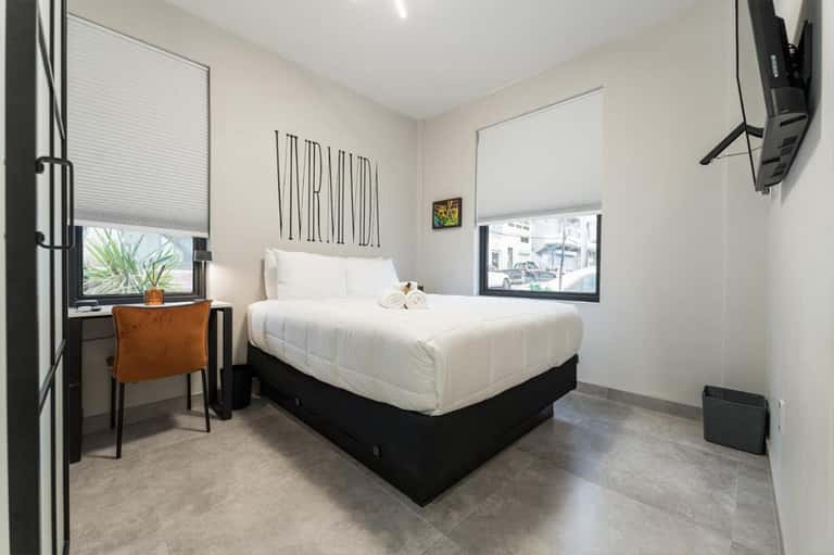 Minimalist hotel bedroom with white bedding, small desk, and window views