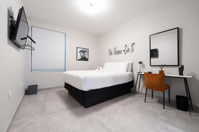 Minimalist hotel room with white bed, desk, flat-screen TV, and contemporary artwork on wall
