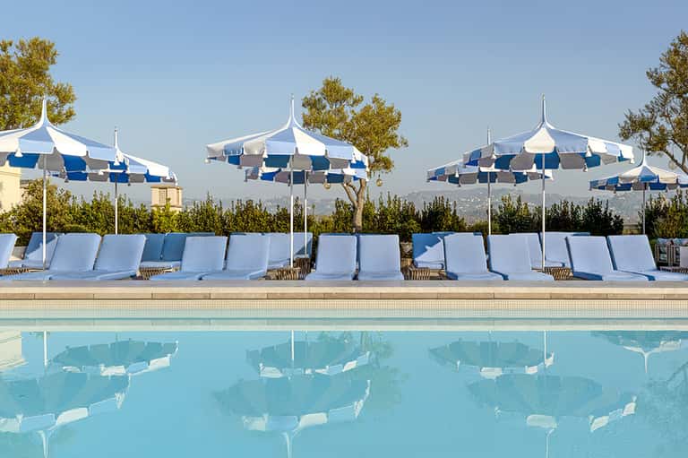 Resort pool with blue and white striped umbrellas, white lounge chairs, and mountain views in background