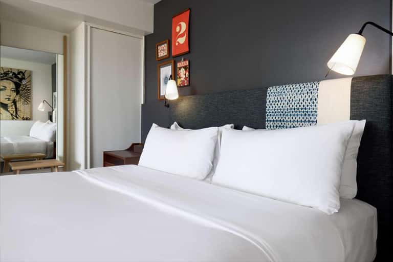 Hotel bedroom with dark accent wall, white bedding, pendant lamps, and ensuite bathroom visible through doorway