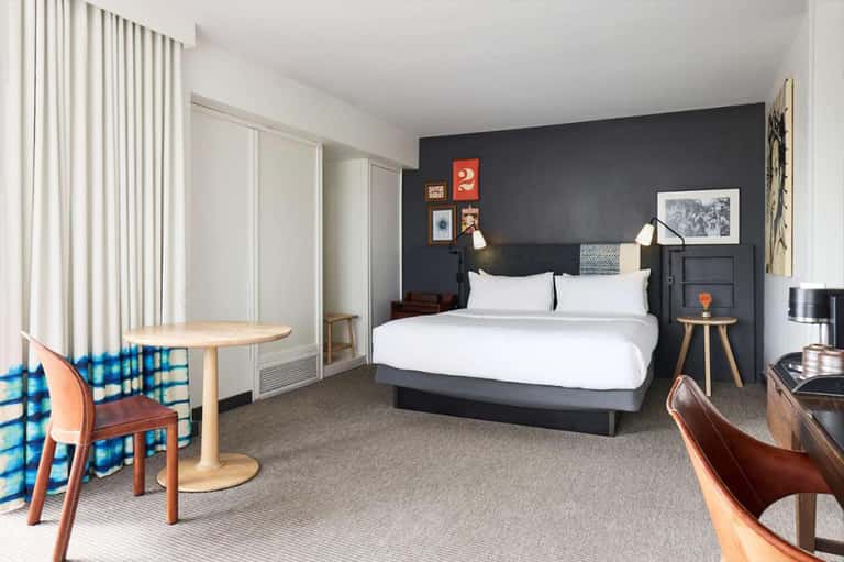 Contemporary hotel bedroom with dark accent wall, white bedding, and mid-century modern furnishings