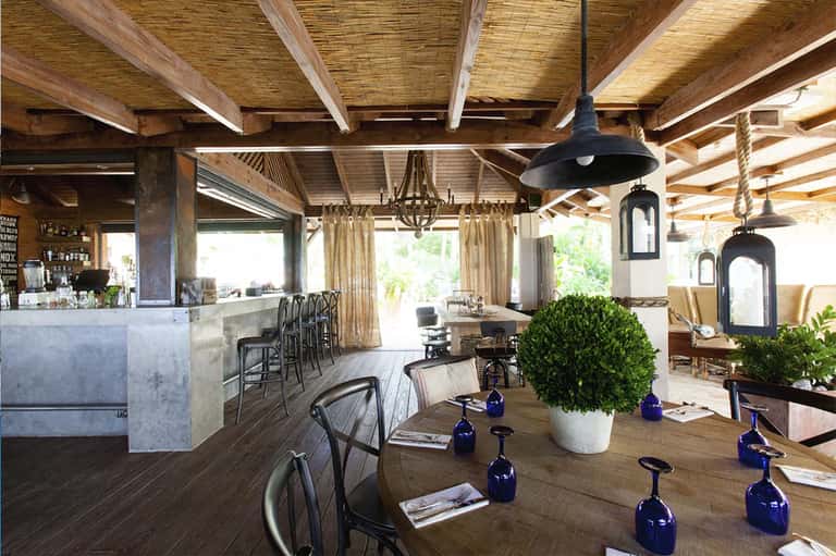 Modern resort restaurant and bar with wooden ceiling beams, black pendant lights, and ocean view access