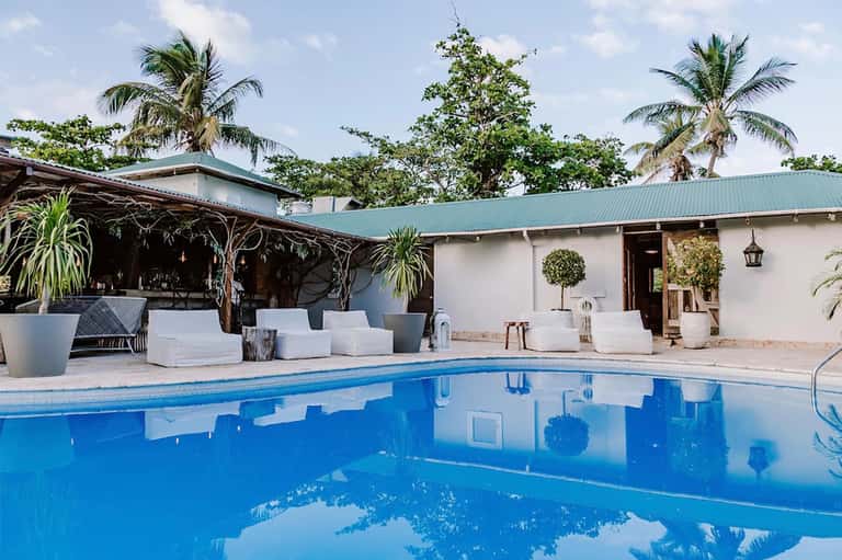 Resort pool with turquoise water, palm trees, white lounge chairs, and covered pavilion area