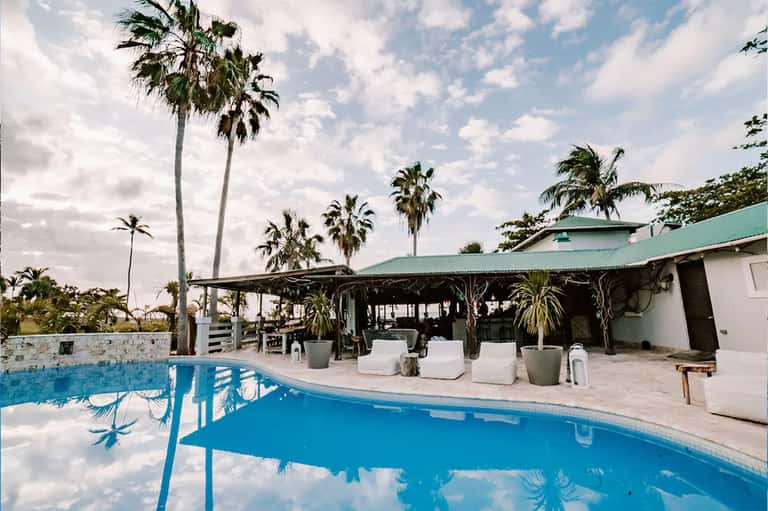 Blue pool with palm trees and covered cabana area under bright sky