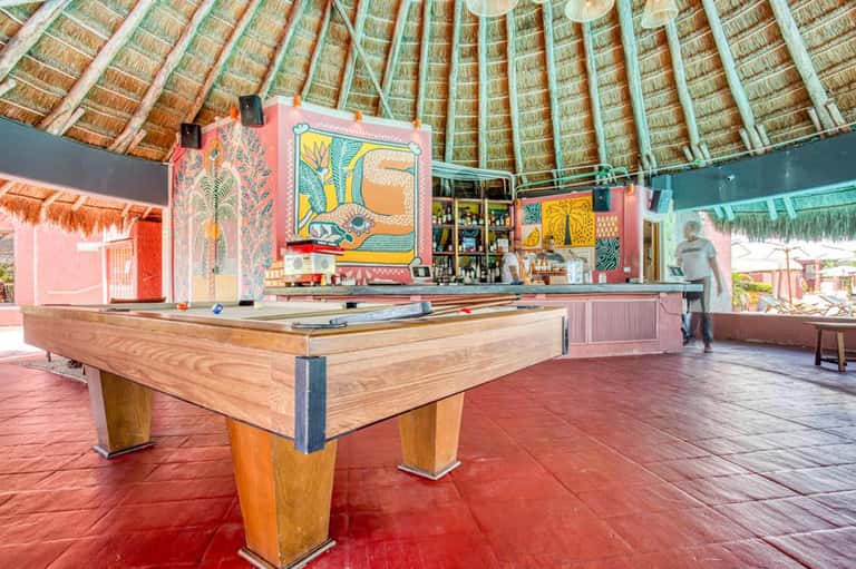 Colorful beach bar interior with pool table, thatched roof, and tropical artwork