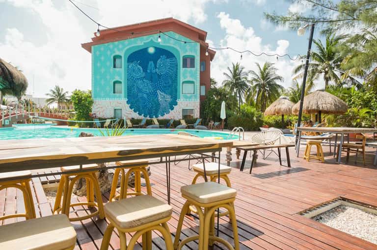 Tropical resort pool with turquoise building featuring peacock mural and palm trees