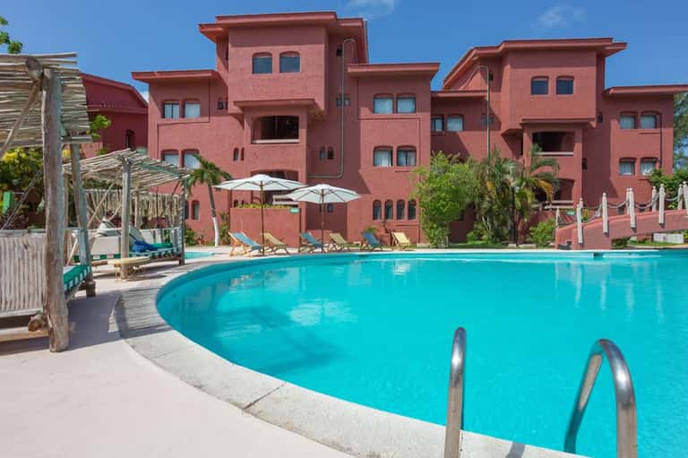 Large turquoise pool with red-orange hotel buildings, umbrellas, and lounge chairs